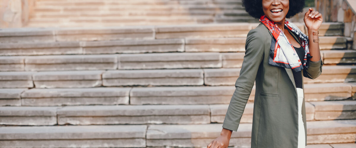 Fashionable girl in a summer city. Black lady in a green jacket. Woman in a red scarf. Famale with sunglasses