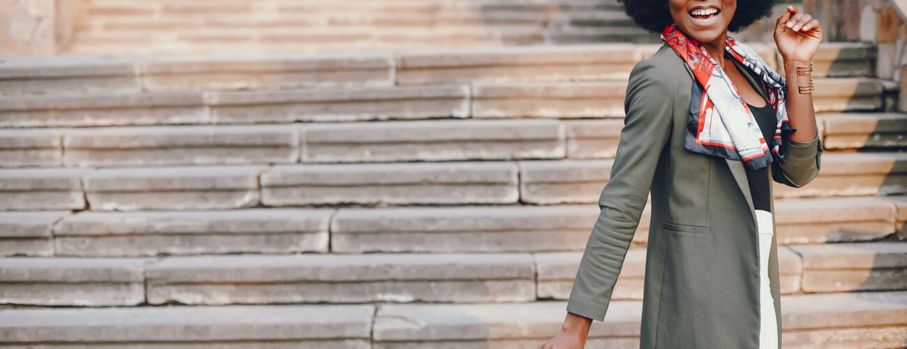 Fashionable girl in a summer city. Black lady in a green jacket. Woman in a red scarf. Famale with sunglasses